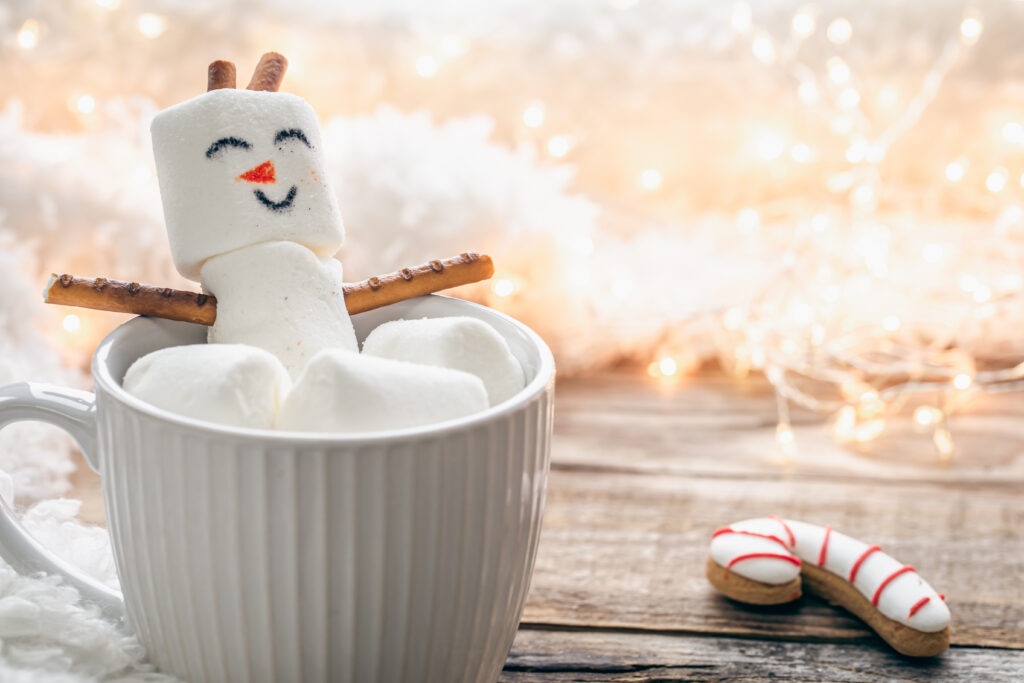 Close up, mug of hot drink with marshmallow snowman on blurred background.